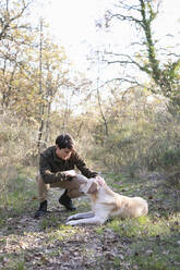 Man stroking Labrador Retriever in forest - EIF02494