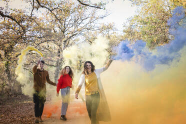 Cheerful friends having fun with smoke flares in autumn forest on weekend - EIF02497