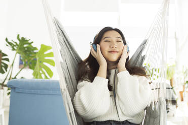 Woman listening music through headphones on hammock - JCCMF04698