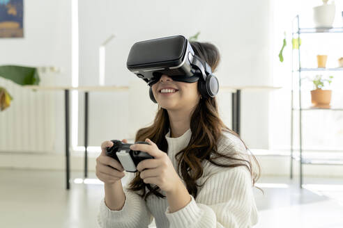 Lächelnde Frau mit Game-Controller und Virtual-Reality-Headset zu Hause - JCCMF04704