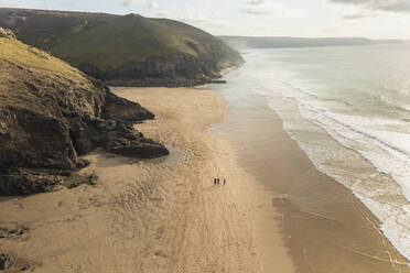 Luftaufnahme von ein paar Personen, die am Strand entlang der Küste in der Nähe des Ozeans spazieren gehen, St Agnes, Cornwall, Vereinigtes Königreich. - AAEF13513