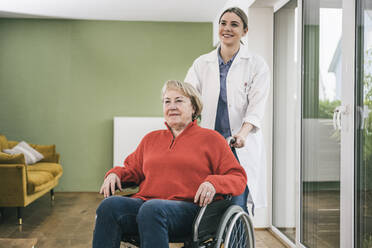 Smiling nurse standing behind disabled patient at home - UUF25105