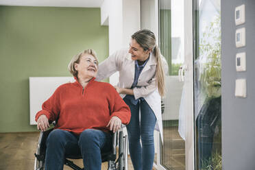 Smiling patient looking at nurse standing by wheelchair - UUF25106