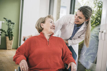 Disabled woman smiling at nurse standing behind - UUF25107