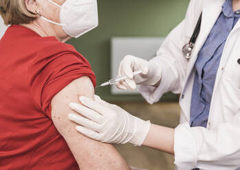 Doctor vaccinating woman wearing face mask at home - UUF25110