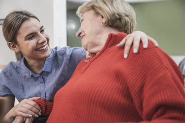 Lächelnde Pflegehelferin mit Arm um den Patienten zu Hause - UUF25117