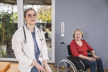 Lächelnder Arzt sitzt mit behinderter Frau im Hintergrund zu Hause - UUF25119