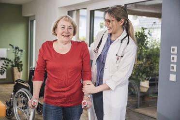 Senior woman with crutches standing by doctor at home - UUF25124