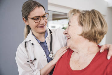 Smiling doctor with hands on patient's shoulders at home - UUF25126