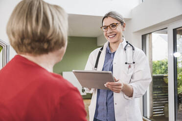 Healthcare worker with tablet PC talking to patient at home - UUF25129