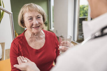 Doctor giving medicine to senior woman at home - UUF25134