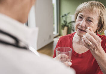 Senior woman showing medicine to doctor at home - UUF25136