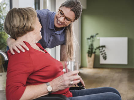 Lächelnde Betreuerin schaut auf eine behinderte Frau im Rollstuhl - UUF25138