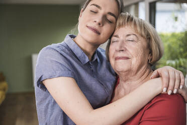 Lächelnde Pflegehelferin und Frau umarmen sich zu Hause - UUF25142