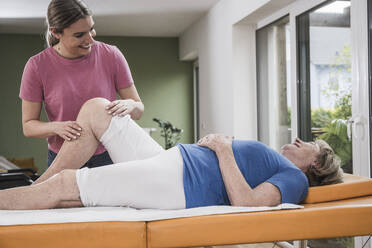 Lächelnde Physiotherapeutin massiert das Knie einer behinderten Frau auf dem Massagetisch - UUF25157