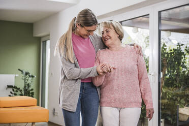 Lächelnde Frau, die mit Hilfe eines Pflegers zu Hause steht - UUF25168