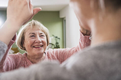 Lächelnde ältere Frau gibt der Krankenschwester zu Hause ein High Five - UUF25179