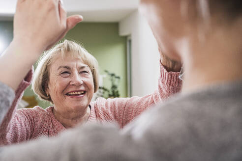 Smiling senior woman giving high five to nurse at home - UUF25179