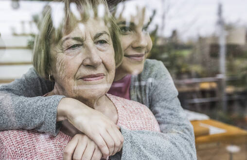 Caregiver hugging senior woman at window - UUF25182
