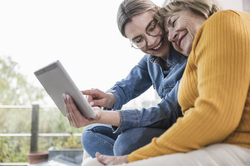 Lächelnde Betreuerin mit Tablet-PC bei einer älteren Frau zu Hause - UUF25184