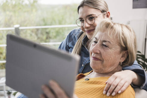 Lächelnde Frauen bei einem Videoanruf über einen Tablet-PC zu Hause - UUF25186