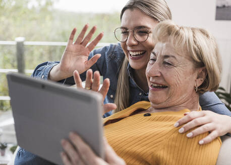 Lächelnde Frauen winken mit der Hand zum Videoanruf über einen Tablet-PC zu Hause - UUF25187