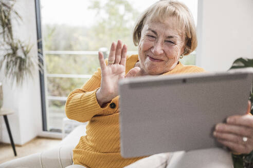 Lächelnde Frau mit winkender Hand bei einem Videoanruf über einen Tablet-PC zu Hause - UUF25188