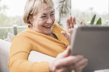 Glückliche Frau winkt mit der Hand zu einem Videoanruf über einen Tablet-PC zu Hause - UUF25189