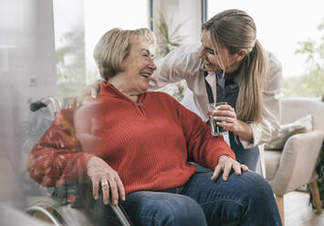 Young nurse giving drinking glass to disabled woman at home - UUF25199