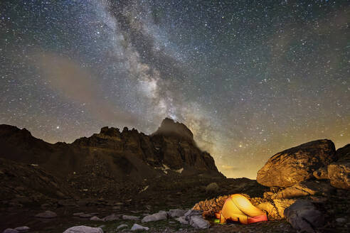 Milchstraßengalaxie, die sich am Nachthimmel über einem einzelnen beleuchteten Zelt im Maira-Tal erstreckt - ANSF00132