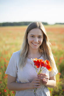 Junge Frau hält Mohnblumen auf einem Feld - BFRF02396