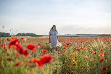 Junge Frau geht inmitten von Mohnblumen auf einem Feld - BFRF02397