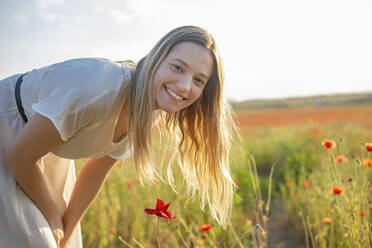 Lächelnde blonde Frau neben Mohnblumen auf einem Feld - BFRF02398