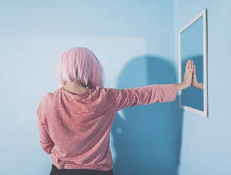 Frau mit rosa Haaren berührt Spiegel an blauer Wand - SVCF00052