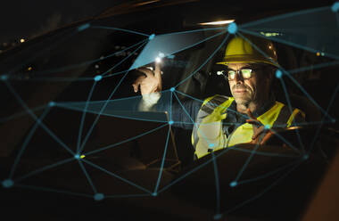 Ingenieur mit Schutzhelm bei der Arbeit an einer beleuchteten Grafik im Auto - UUF25208
