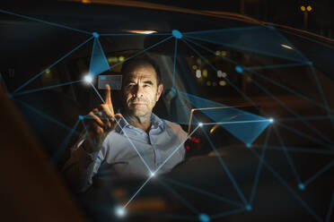 Businessman working on futuristic graph in car at night - UUF25210