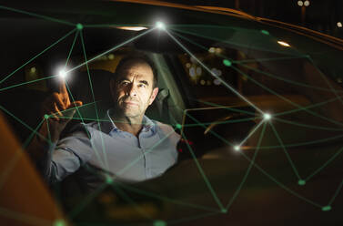 Businessman working on digitalized graph in car at night - UUF25212