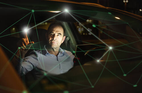 Geschäftsmann bei der Arbeit an einer digitalisierten Grafik im Auto bei Nacht - UUF25212