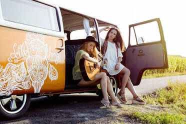 Zwei hübsche Mädchen in Sommerkleidung haben Spaß vor einem Lieferwagen und spielen Gitarre - ADSF32203