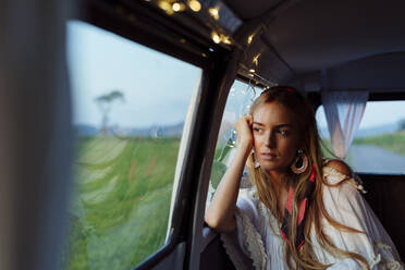 Confident beautiful blonde girl leaning on the window inside a vintage van looking away - ADSF32206