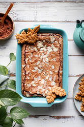 Draufsicht auf einen leckeren gebackenen Brownie mit Mandelblättchen in einem Backblech mit Keksen auf einem Holztisch mit Kakaopulver - ADSF32236