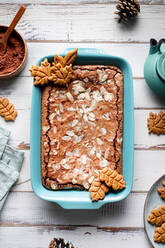 Draufsicht auf einen leckeren gebackenen Brownie mit Mandelblättchen in einem Backblech mit Keksen auf einem Holztisch mit Kakaopulver - ADSF32237