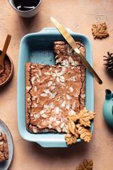 Draufsicht auf einen leckeren gebackenen Brownie mit Mandelblättchen in einem Backblech mit Keksen auf einem Tisch mit Kakaopulver - ADSF32238