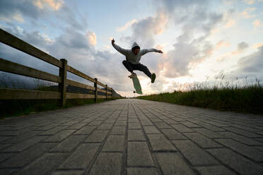 Ground level of full body of male in casual wear performing stunt on longboard on paved walkway - ADSF32243