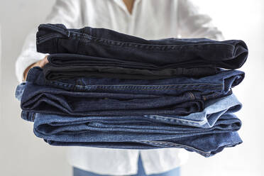 Crop anonymous female in white shirt with stack of blue jeans in hands - ADSF32259