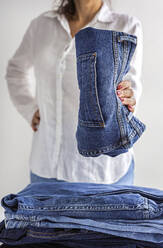 Crop anonymous female in white shirt with stack of blue jeans in hands - ADSF32260