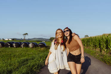 Zwei glückliche Freundinnen in Sommerkleidung, die sich an einem sonnigen Tag vor einem alten Lieferwagen amüsieren - ADSF32288