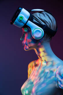 Weibliche Schaufensterpuppe mit VR-Headset steht unter heller mehrfarbiger Beleuchtung vor violettem Hintergrund - ADSF32306
