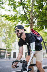 Seitenansicht eines bärtigen männlichen Hipsters mit künstlichem Arm, der im Sommer in der Stadt Fahrrad fährt - ADSF32370