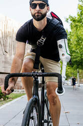 Bärtiger männlicher Hipster mit künstlichem Arm, der im Sommer in der Stadt Fahrrad fährt - ADSF32371